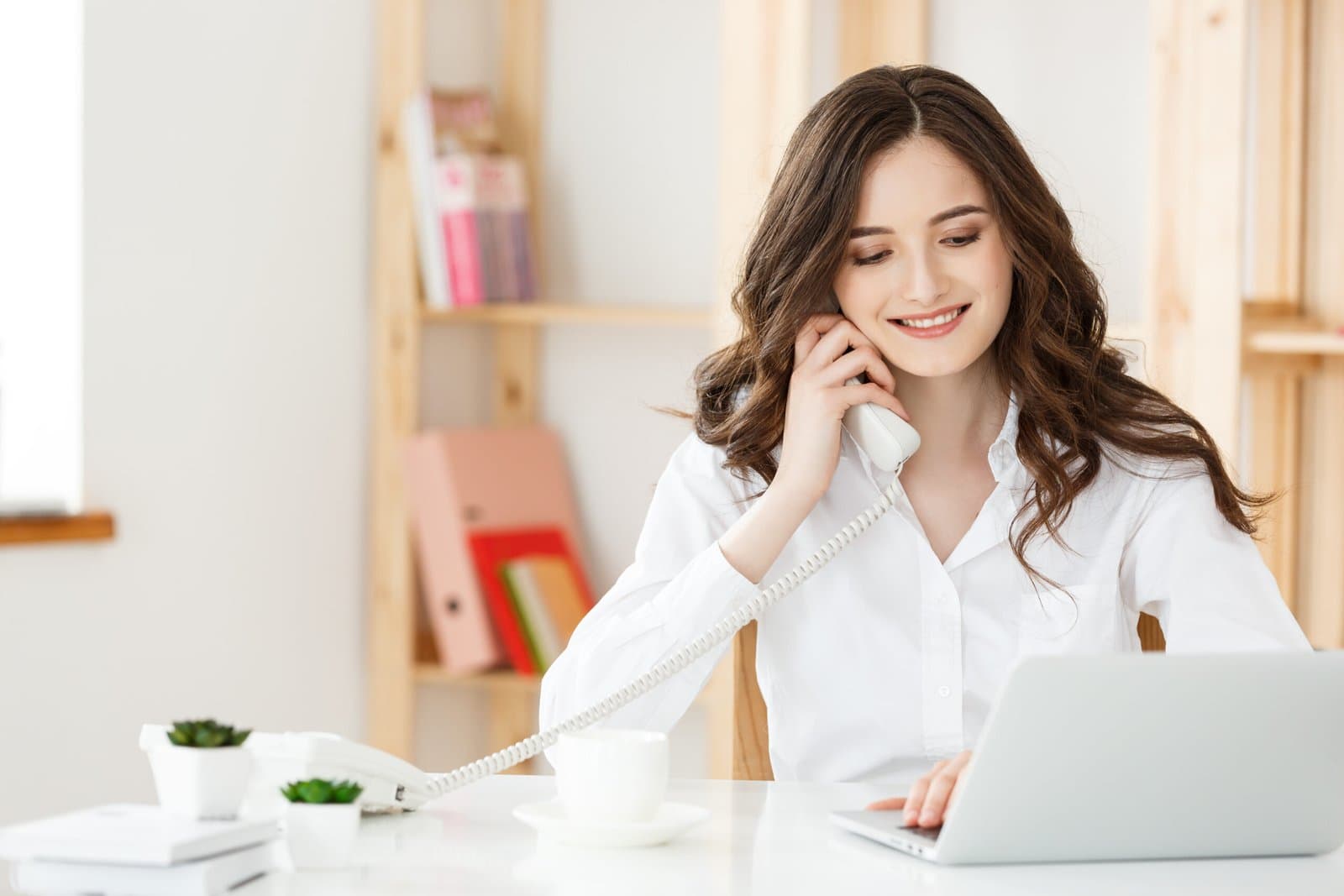 Young businesswoman or secretary sitting at desk and working, smiling and looking at camera