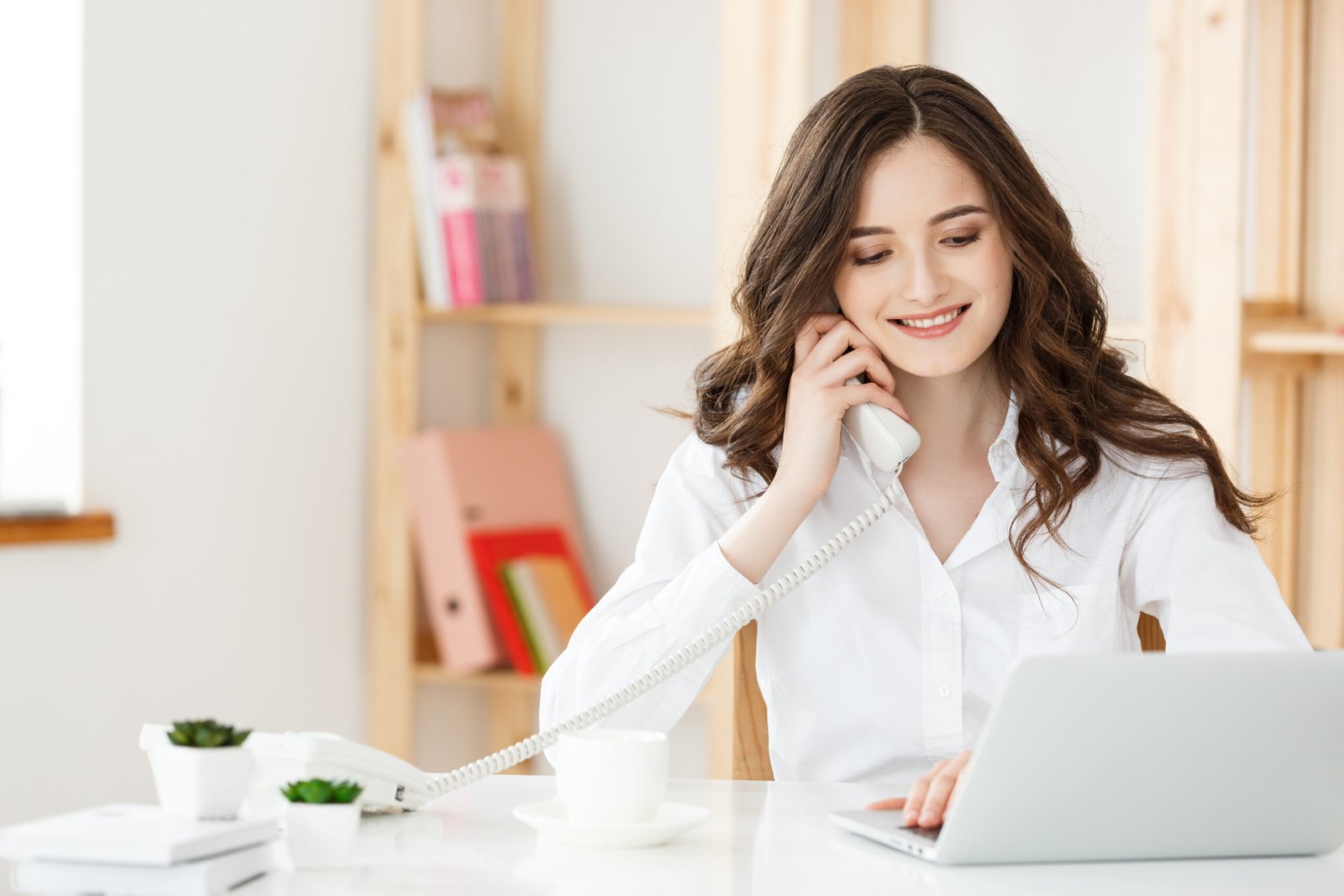 Young businesswoman or secretary sitting at desk and working. Smiling and looking at camera.